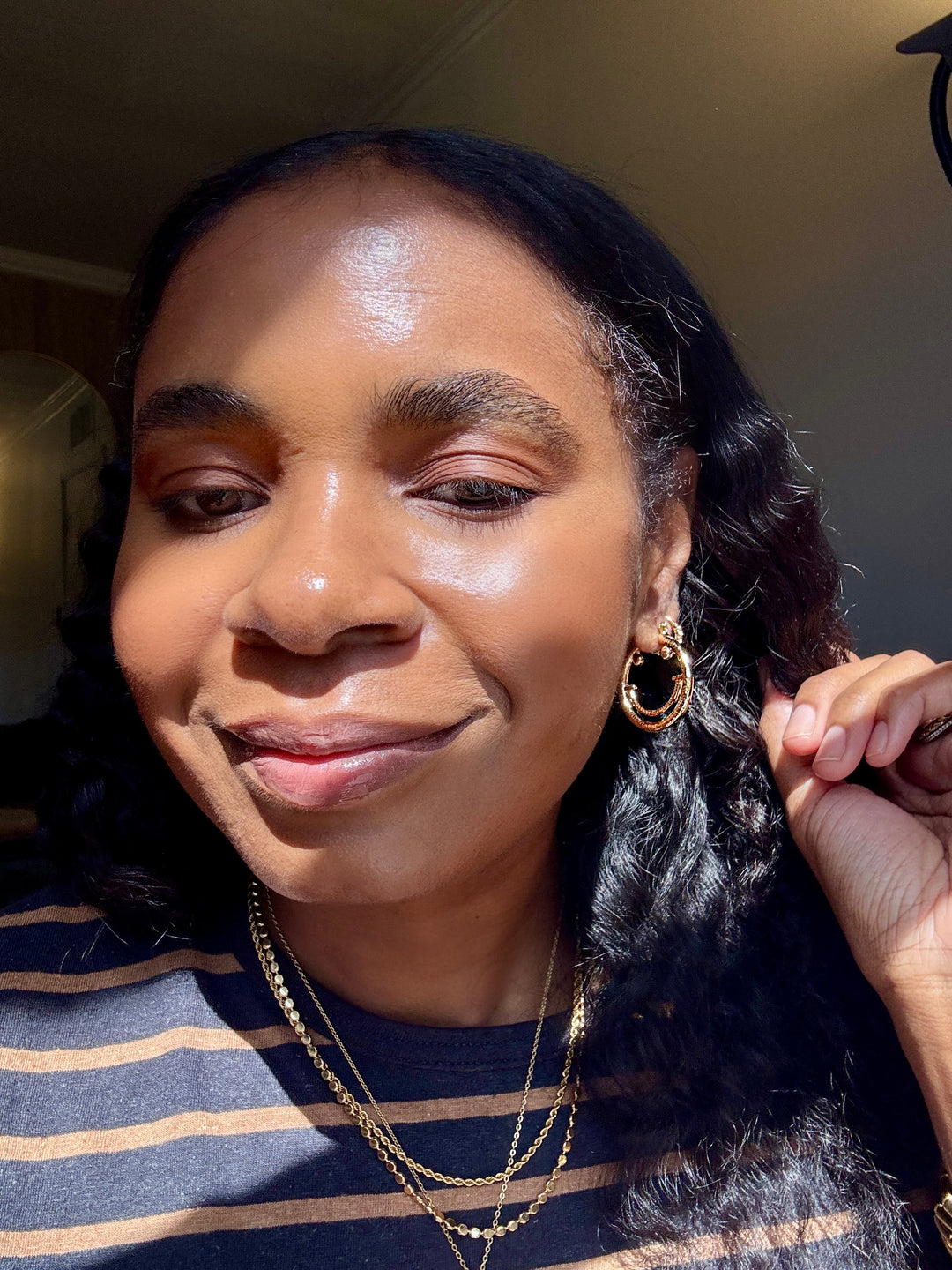 Woman with styled hair and small smiley face gold hoops jewelry indoors