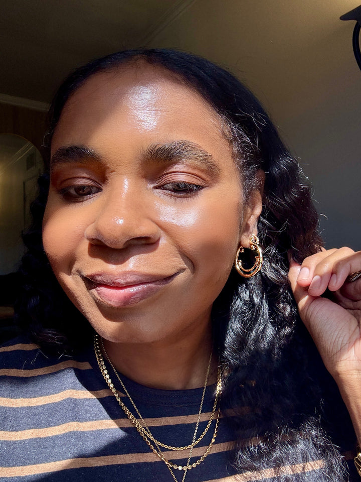 Woman with styled hair and small smiley face gold hoops jewelry indoors